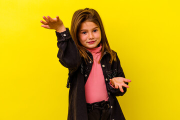 Little caucasian girl isolated on yellow background makes scale with arms, feels happy and...