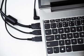 Gray laptop with connected wires in interface on white table. View from above.