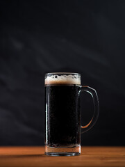 Beer mug of fresh stout on a wooden table, dark background copy space