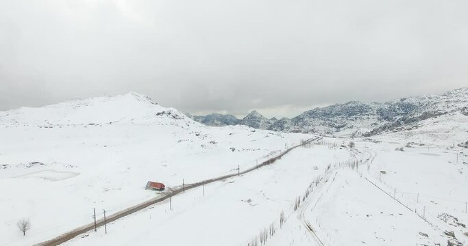 Beautiful aerial view of mountains covered by snow in foggy weather after a snowstorm. Cloudy weather and mountains covered with thick layer of snow. Frozen trees and lakes. Empty road