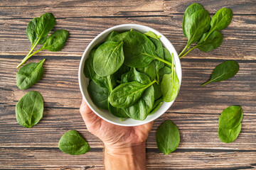 Fresh Organic Healthy Spinach in White Bowl Overhead Shot with White Male Hands Holding White Bowl on Wood Texture Table Background