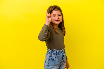 Little caucasian girl isolated on yellow background joyful and carefree showing a peace symbol with...