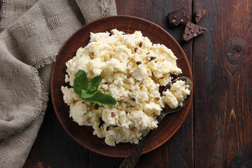 Fermented milk product. Cottage cheese  with chocolate in a clay plate on an old wooden background. Curd mass with mint and spoon. Rustic. Flatlay, top view. Background image, copy space