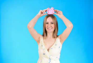 Young woman holding alarm clock on head standing over isolated blue background very happy