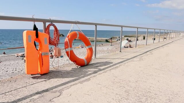 Life-saving equipment on beach for people. Orange lifebuoy, life jacket and rope