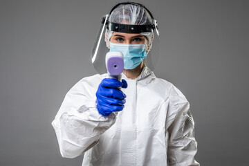 male doctor wearing protective clothing, glasses, mask and gloves, with a non-contact thermometer to measure temperature, on a white background. Coronavirus epidemic concept
