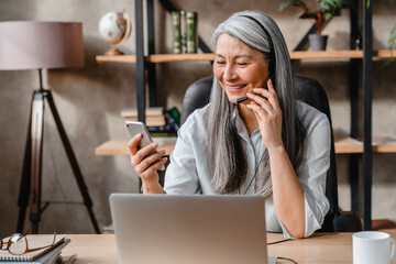 Cheerful middle-aged caucasian woman hot line worker using smart phone at work place