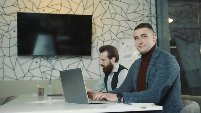 An image of two programmers working on a laptop and a tablet. Web programmers at remote work. Man's gaze at the camera.