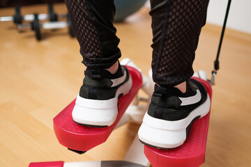 Back view on the woman feet in sneakers doing exercising on the twist stepper or stair stepper...