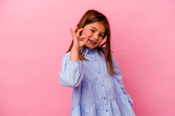 Little caucasian girl isolated on pink background  winks an eye and holds an okay gesture with hand.