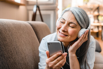 Dreamy caucasian mature woman listening to the music on the sofa in the living room