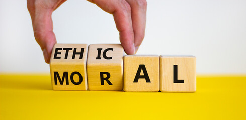 Ethical or moral symbol. Businessman turns wooden cubes and changes the word 'moral' to 'ethical' on a beautiful yellow table, white background. Business and ethical or moral concept. Copy space.