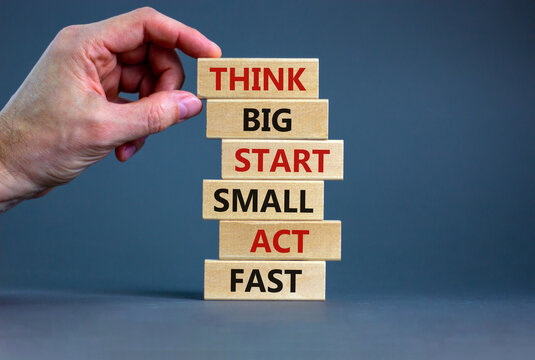 Think big start small symbol. Words 'Think big start small act fast' on wooden blocks on a beautiful grey background. Businessman hand. Business, motivational and think big start small concept.