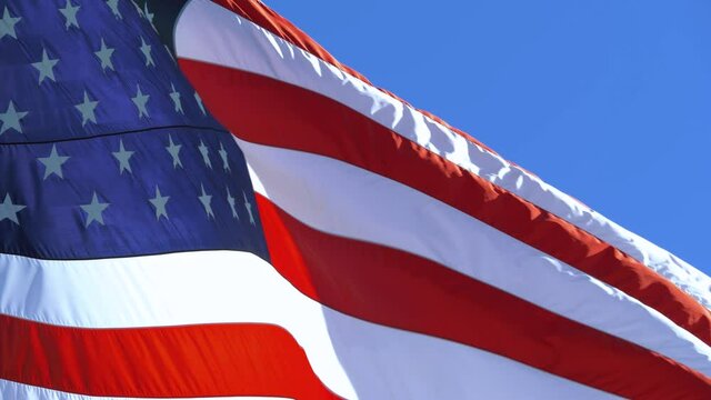 Copy space on a blue sky background. USA flag flaping in wind. Close-up of an American flag flying in the wind against a background of clear sky. Close up of American flag waving. Slow motion, closeup