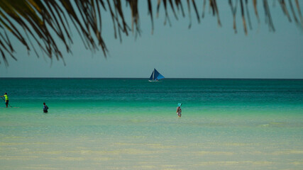 Tourists on a sandy beach and blue sea through palm branches. Summer and travel vacation concept....
