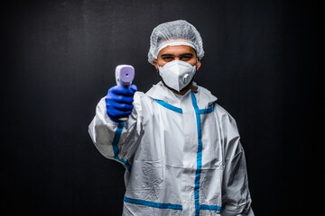 Fototapeta na wymiar Biological hazard. Confident and serious doctor in protective suit and face mask holding infrared measuring tool , standing against black background