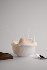 splash of milk in a plate on the table with chocolate and a spoon on white background. selective focus 