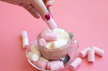 transparent cup with cocoa on pink background with marshmallows