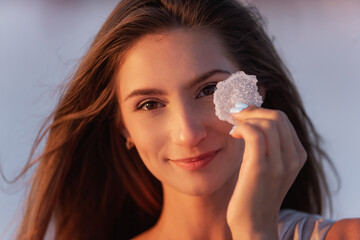 Close-up portrait of a young blonde woman holding a piece of crystallized white salt in her hands....