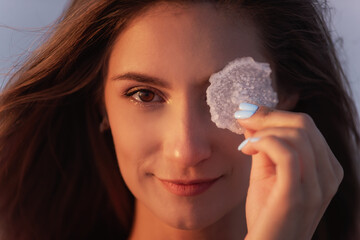 Close-up portrait of a young blonde woman holding a piece of crystallized white salt in her hands....