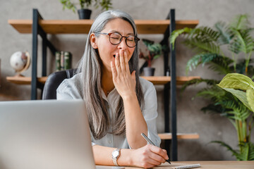 Bored after working day in office mature grey-haired woman sitting at the desk