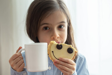 A little girl holds cookies and a cup of milk in her hands close up.