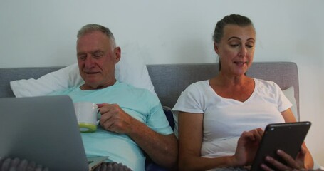 Caucasian senior couple using laptop and digital tablet in bed at home - Powered by Adobe