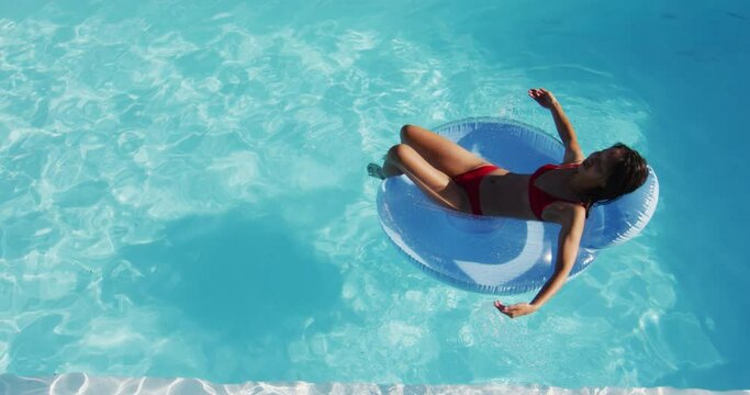 Mixed race woman having fun sunbathing on inflatable in swimming pool