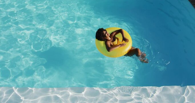 Mixed race woman having fun sunbathing on inflatable in swimming pool