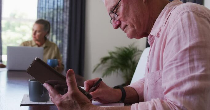 Caucasian senior taking notes while using digital tablet at home