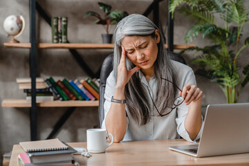 Tired mature caucasian woman having headache after hard work in office