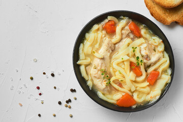 Homemade chicken noodle soup with vegetables and spices in a bowl, top view, white concrete background. Healthy food concept