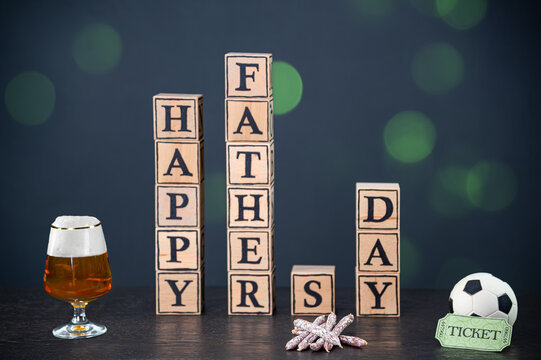 Gift Ideas For Fathers Day. A Cold Beer, Small Salamis For The Fathers Day Tour Or A Ticket For A Soccer Match. In The Background Are Wooden Cubes To The English Text: Happy Father's Day.