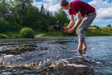 A male videographer walks on the water and films the current of the river. A photographer in a red T-shirt films as a stream of water rushes down.