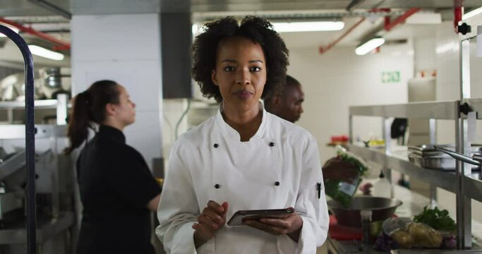 Portrait of african american female chef holding tablet looking at camera and smiling