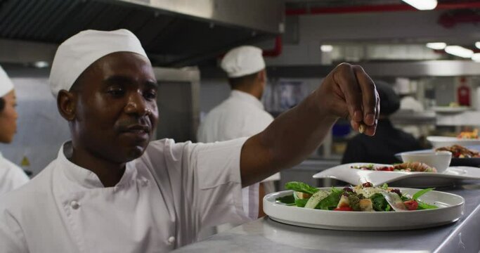 African american male chef garnishing dish and similing in restaurant kitchen
