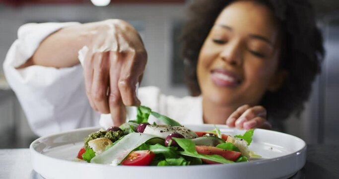 African american female chef garnishing dish and similing in restaurant kitchen