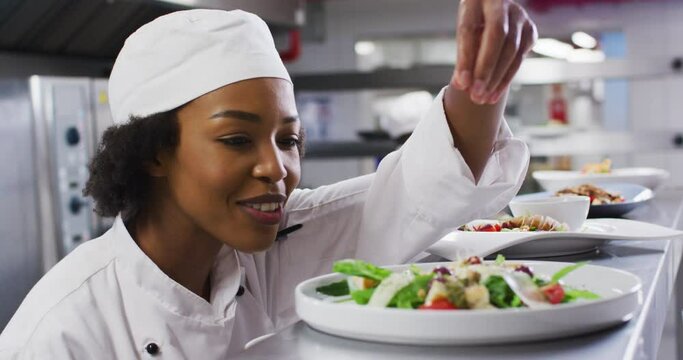 African american female chef garnishing dish and similing in restaurant kitchen