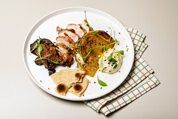 Duck breast with cabbage steak, cheese sauce and rye flatbread. Delicious restaurant dish on a round plate on a checkered napkin