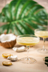 banana cocktail with coconut milk in a glass on light beige background with palm leaves