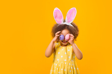 An african girl with rabbit ears on her head with painted eggs in her hands on a yellow background.