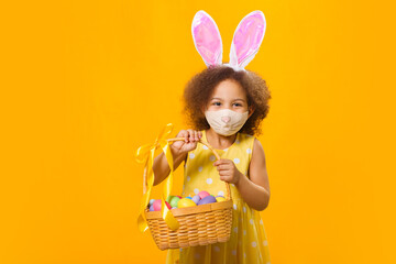 A cheerful african girl with rabbit ears on her head and a protective mask with a basket of colored eggs in her hands