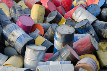 Randomly stacked yellow, blue, black, red metal drums for fuel.