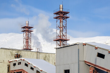Factory buildings and two chimneys against the background of snowy mountains and blue sky.