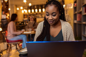 Fototapeta premium Portrait of young African woman using laptop in coffee shop