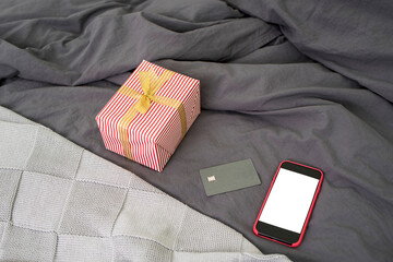 A mobile phone with a white screen and a place for text, office glasses, debit card, notepad, on a bed with grey linen and plaid. Online shopping.