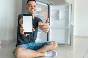 A young guy orders food using a smartphone. Empty refrigerator with no food. Food delivery service advertisement