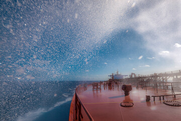 Sea water splashes on bow area of super tanker proceeding by ocean