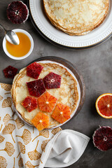 Thin pancakes with honey and blood oranges on a gray table. Treats at the Maslenitsa.