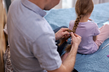 rear view on careful young father braiding hair of daughter. Happy Father's day. focus on child...
